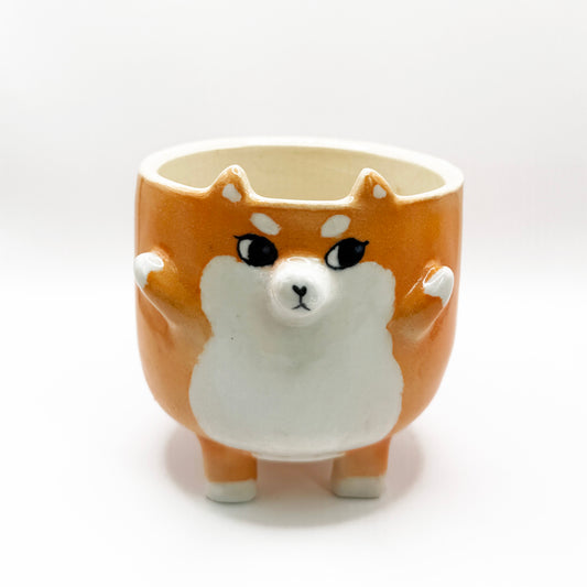 Orange colored shiba inu mug with side eyes. The shiba's two hands are up and it has a tail on the bottom of the mug