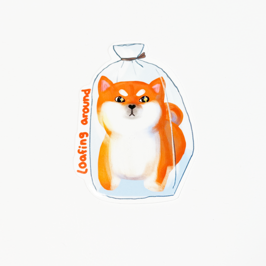 A die-cut sticker featuring an illustration of an orange and white Shiba Inu dog inside a clear plastic bag with the text 'loafing around' written vertically in orange, shown on a plain white background.
